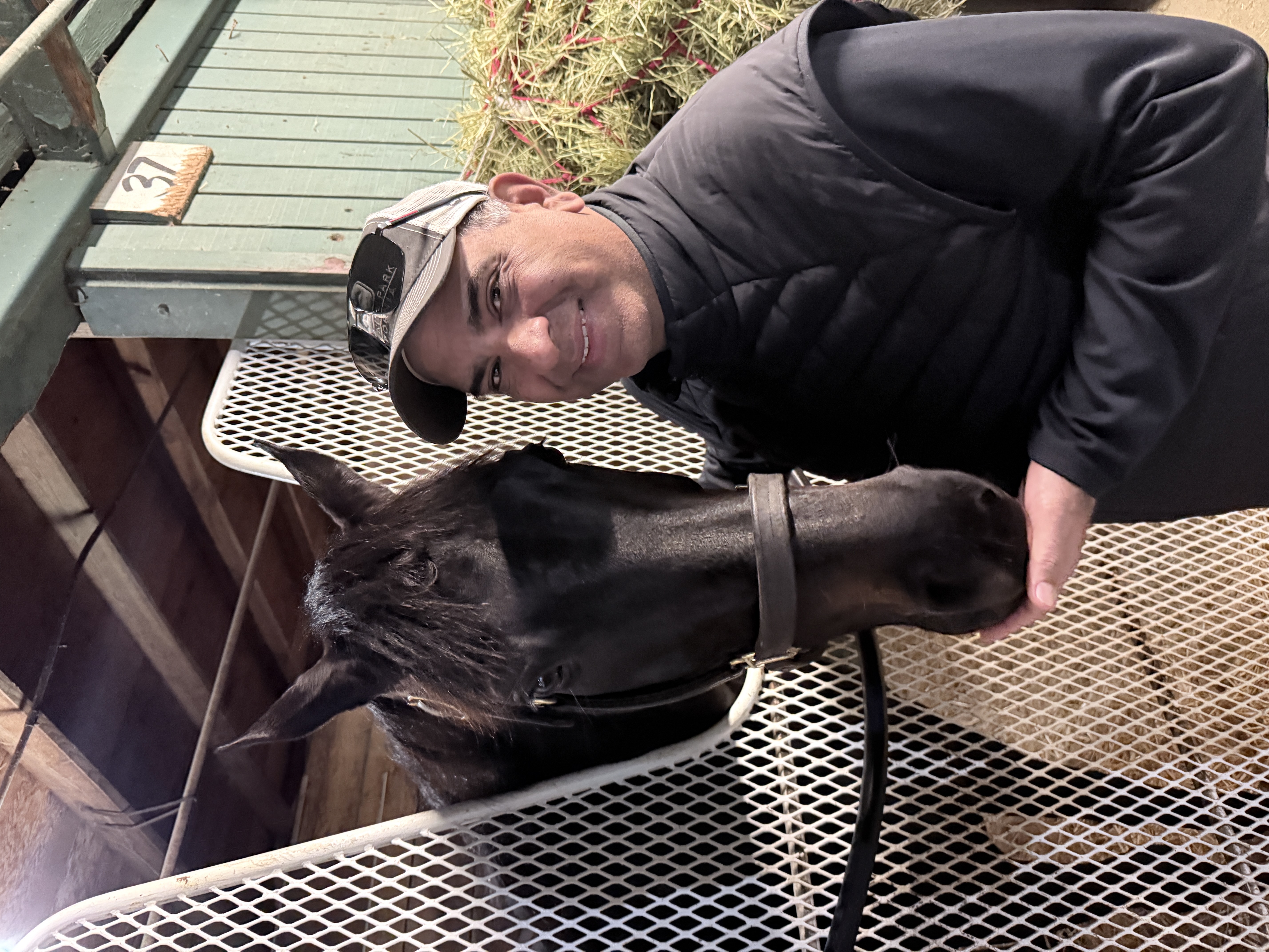 A man smiling beside a dark horse at the stable